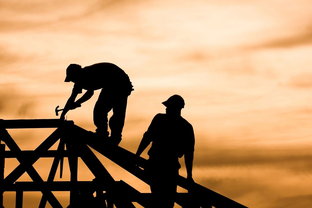 qtq80-Ln1o51 Two construction workers are silhouetted on roof scaffolding.